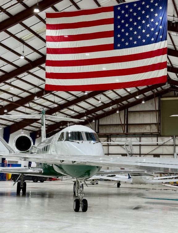 Private jet parked beneath a large American flag inside a Kansas City hangar