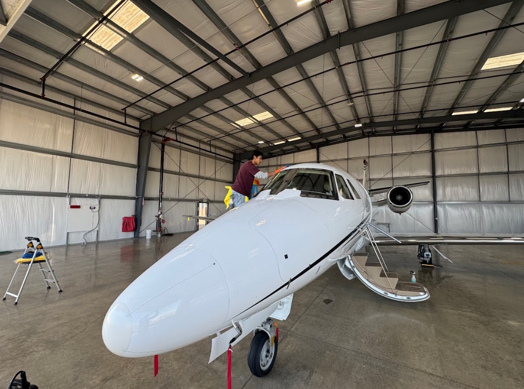 Technician cleaning the exterior of a white private jet inside a Kansas City hangar